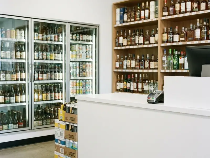 Liquor store checkout counter with a card terminal, spirits shelves and beer coolers